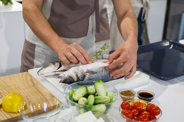 Chief putting thyme in raw fish before cooking in light kitchen. Preparing trout for baking in...