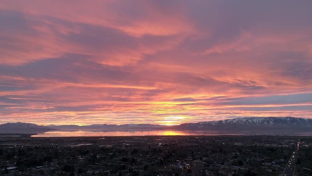 Aerial view flying backwards over town during colorful sunset in Utah over Orem viewing Utah Lake.