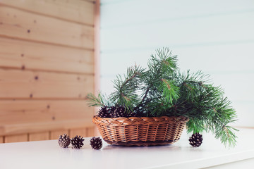 Green pine branches in a wicker basket on a white chest of drawers on a wooden background