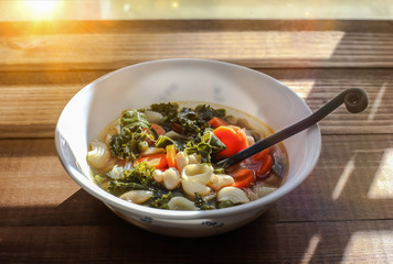 Vegetables soup on wooden table with sun behind