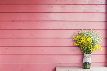  Home decor. Wildflowers in a vase on a background of wooden pink boards.