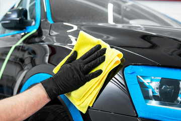 Car polish wax worker hands applying protective tape before polishing. Buffing and polishing car. Car detailing. Man holds a polisher in the hand and polishes the car. Tools for polishing
