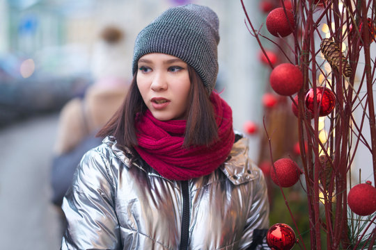 portrait of a beautiful girl on the street with new-year decorations in red colors. balls and branches, Christmas tree branches.