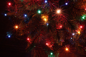 Fototapeta na wymiar Christmas tree part with snowflakes and garland with reddish green, blue, pink and orange lights, formed like beamons on dark background