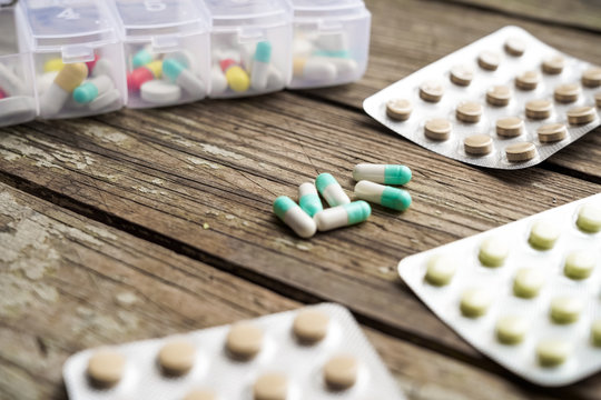 Variety of pills in white plastic pill organizer on weathered wood