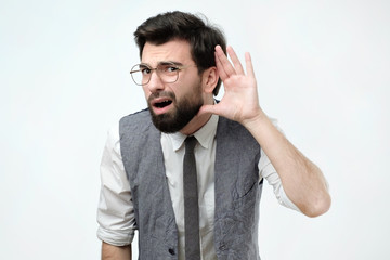Closeup portrait of curious or deaf man placing hand on ear asking someone to speak up or listening...