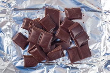 Several pieces of chocolate of the variety bittersweet lie on a silver paper