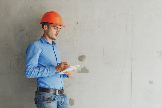 Construction supervisor writes on notebook near the wall. Handsome foreman taking notes in clipboard. Construction inspector checking new object