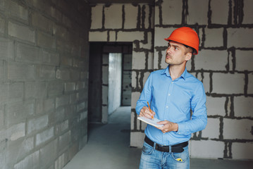 Construction supervisor writes on notebook near the wall. Handsome foreman taking notes in...