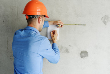 Construction supervisor writes on notebook near the wall. Handsome foreman taking notes in...