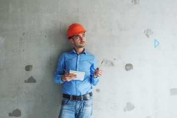 Construction supervisor writes on notebook near the wall. Handsome foreman taking notes in...
