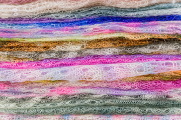 Stack of knitted downy scarfs for background. Russian famous Orenburg shawls. Crochet, pattern.