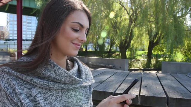 Young millennial beautiful happy busy woman girl outside texting on cellphone mobile smartphone sending messages on social media and updating newsfeed on mobile device with sunflare