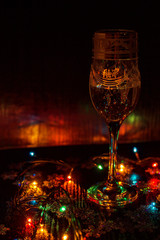 Half full wineglass and garland with red, yellow, green and blue warm lights on dark background