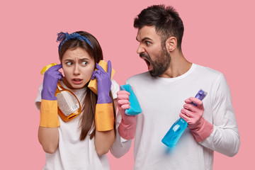 Family, domestic duties and relationship concept. Irritated man with stubble, shouts at wife who plugs ears, do housework together, argue who should clean windows, isolated over pink background