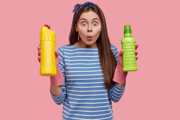 Photo of stupefied Caucasian woman from cleaning service, carries necessary supplies, wears rubber...