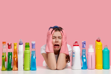 Depressed crying woman looks stressfully, keeps both hands on head, wears protective gloves,...