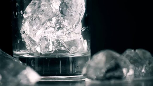 Crystal ice in glass rotating on dark background. Close up 4k footage.