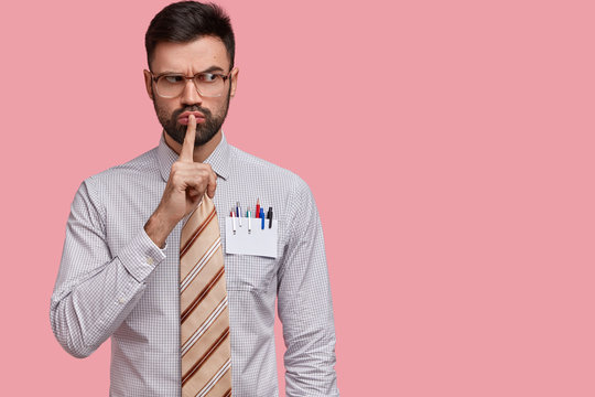 Horizontal Shot Of Serious Male Office Worker Dressed In Formal Shirt And Tie, Demonstrates Shush Sign, Asks Not To Interrupt And Stay Calm, Poses Against Pink Background With Free Space For Your Text