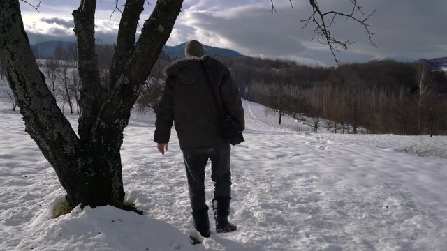 Man touches tree and goes in snow into distance - (4K)