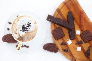 Cup of esspreso or late macciato with whipped cream, cinnamon sticks, cookies and chocolate on snow. Winter refreshment.