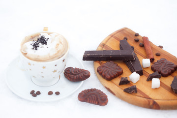 Cup of hot chocolate or coffee with whipped cream, cinnamon sticks, cookies and chocolate on snow. Winter refreshment.