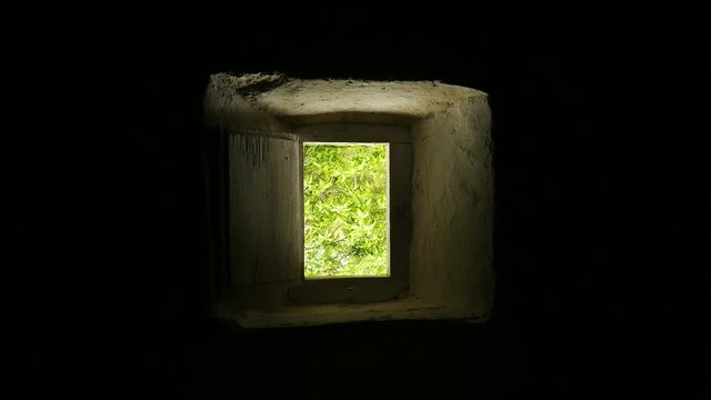  Vista de vegetaci&oacute;n por una peque&ntilde;a ventana de madera desde el interior de una casa rural antigua de adobe