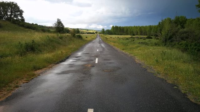 Bello paisaje con carretera recta y mojada por la lluvia un d&iacute;a de tormenta con sol y nubes y arboles y vegetaci&oacute;n verde en primavera