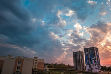 Fototapeta premium evening fluffy curly rolling clouds of awesome sunset against the background of multi-storey apartment buildings