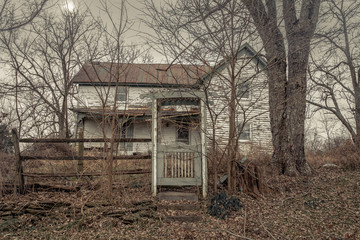 Old gate in front of an abandoned farm house with overgrown grass