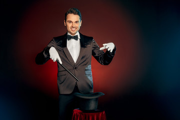 Professional Occupation. Magician in suit and gloves standing isolated on wall holding cane making...
