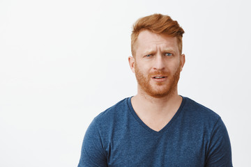 Redhead adult man in stupor cannot understand what happening, feeling clueless and questioned, lifting eyebrow and staring confused at camera, standing uncertain over gray background