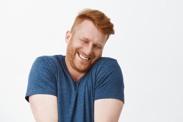 Fototapeta premium Oh stop it you. Portrait of cute pleased and satisfied happy and funny redhead man in blue t-shirt, shrugging and leaning face on shoulder while smiling broadly, blushing from joy and happiness