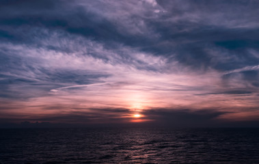 Naklejka na ściany i meble Beautiful dark blue and purple sunset with soft clouds over the ocean. Light of the setting sun reflected on the surface of the calm Caribbean Sea.