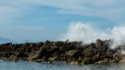 Ocean waves break over a rock wall sending spray into the air. Bright blue sky and clear turquoise water of an island paradise coastal scene.