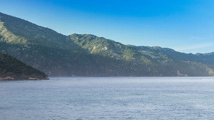 Early morning haze on the mountains rising from the ocean along the coast of Haiti at sunrise.  Sunlight on steep lush green hills at the shore.