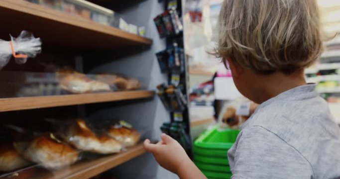 Cute little boy with shopping cart takes bread at market