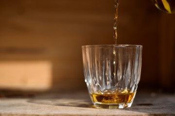 Whiskey drink being poured into a glass against wooden background.