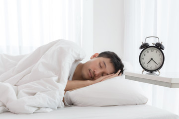 Young asian handsome man sleeping in his bedroom. Boy sleeping with alarm clock in foreground. The time is half pass 7 AM. Wake up in morning of working day concept.
