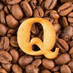 Q, Letter of the alphabet on wood- background of coffee beans.