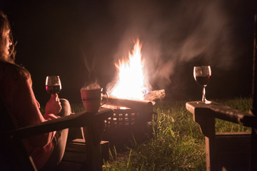 woman looking at en outdoor fire while having a glass of wine