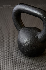 Naklejka na ściany i meble Black kettlebell on a black gym floor, simple commitment to fitness