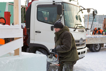 Worker cuts a lump of ice with a chainsaw