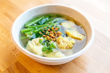 Top view of Wanton soup with morning glory and deep fried garlic in bio paper bowl on wooden background.
