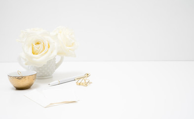 Fototapeta na wymiar White table top female branding set up with white roses gold clips and cold small ring dish