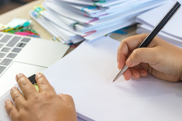 Fototapeta premium Teacher holding pen by hand for checking student homework assignments on desk in school office. Unfinished paperwork stacked in archive with color binder paper clips. Education and business concept.