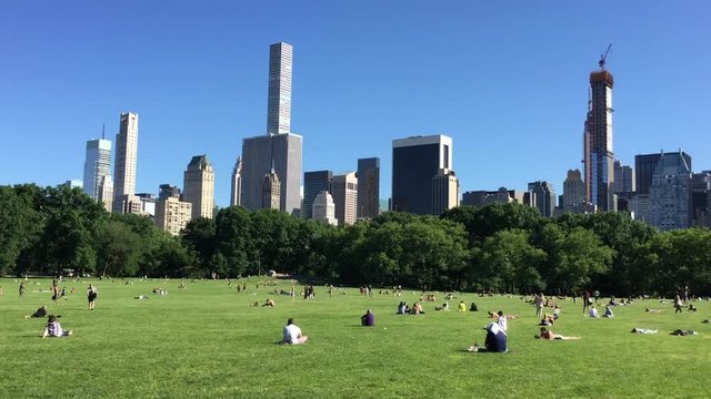 NEW YORK - JUNE 12, 2018: People in Sheep Meadown Central park on sunny day in Manhattan with buildings in background.