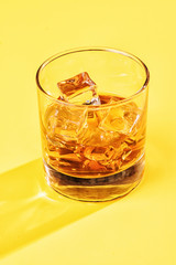 whiskey on the rocks on yellow background tight vertical