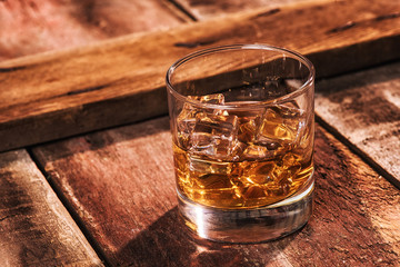 glass of whiskey and ice on wooden table 3/4 view