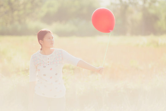 Women walking in rice fields and playing red balloons in their hands